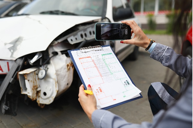 Insurance agent takes pictures of crashed car on his smartphone and fills out the insurance